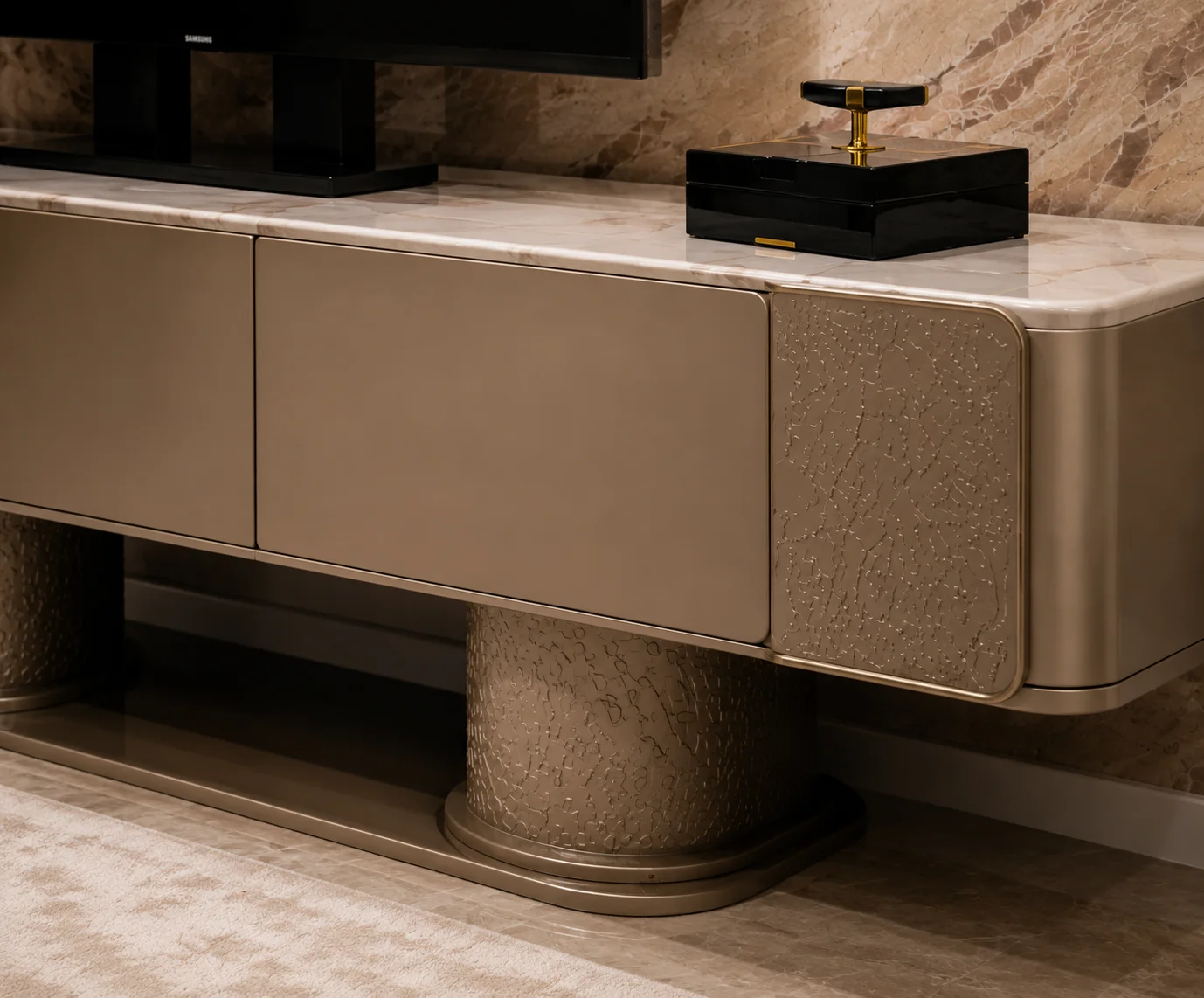 Close-up of the Aspendos TV console showing its pale marble-look top, smooth taupe doors, textured side panel and cylindrical pedestal base